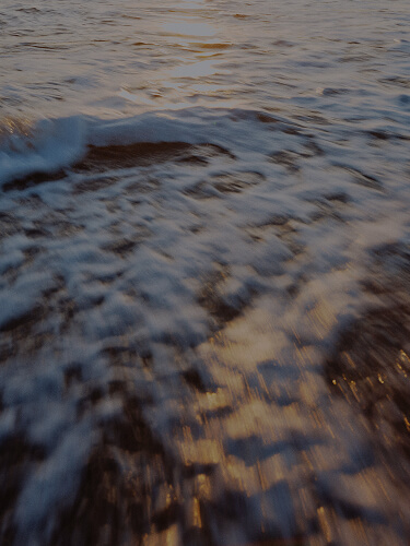 Two cars on a road, one appearing blurred due to motion, viewed from above with shadows on the asphalt.