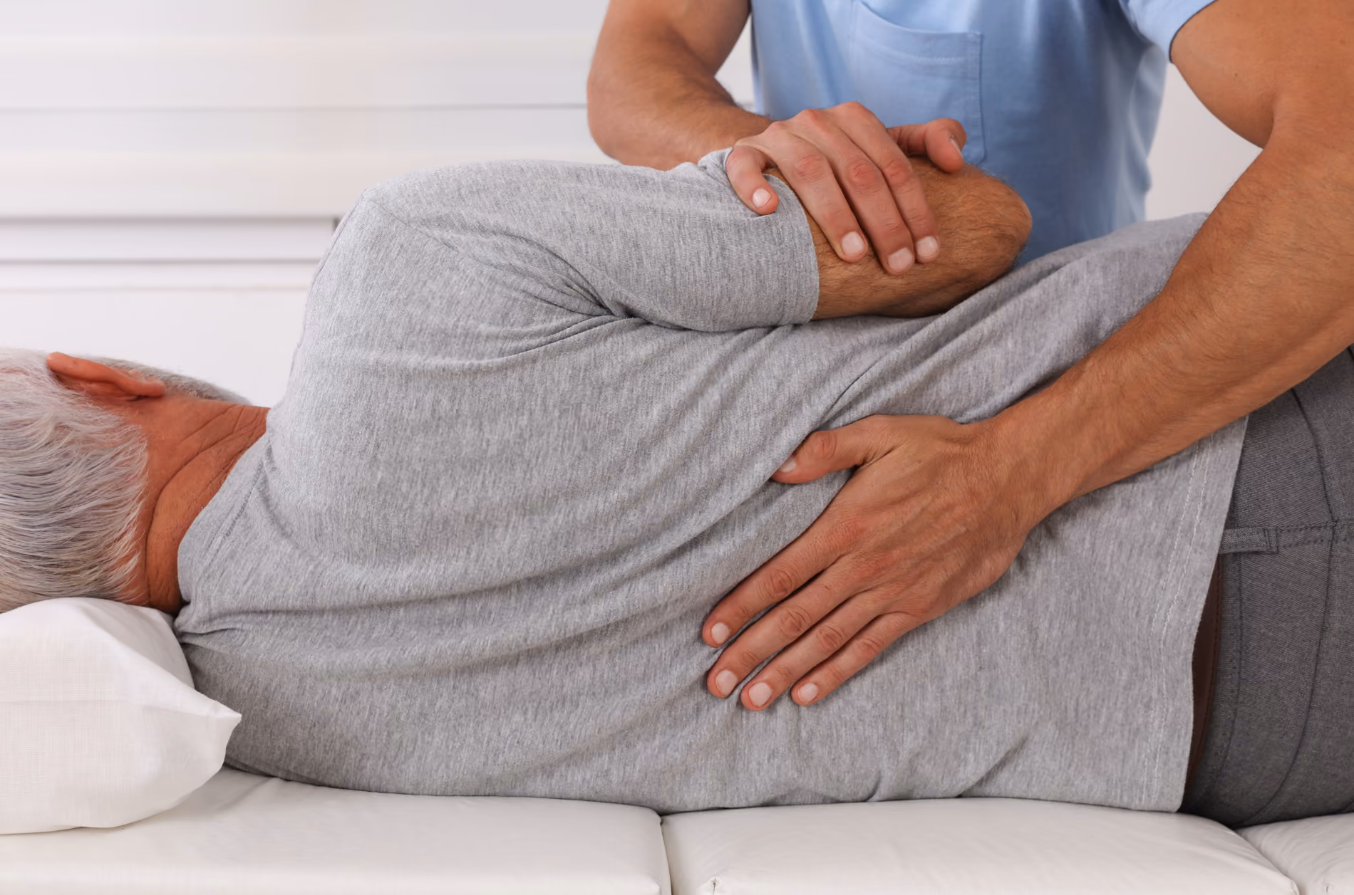 Physiotherapeut mobilisiert die Lendenwirbelsäule eines Patienten in Seitenlage