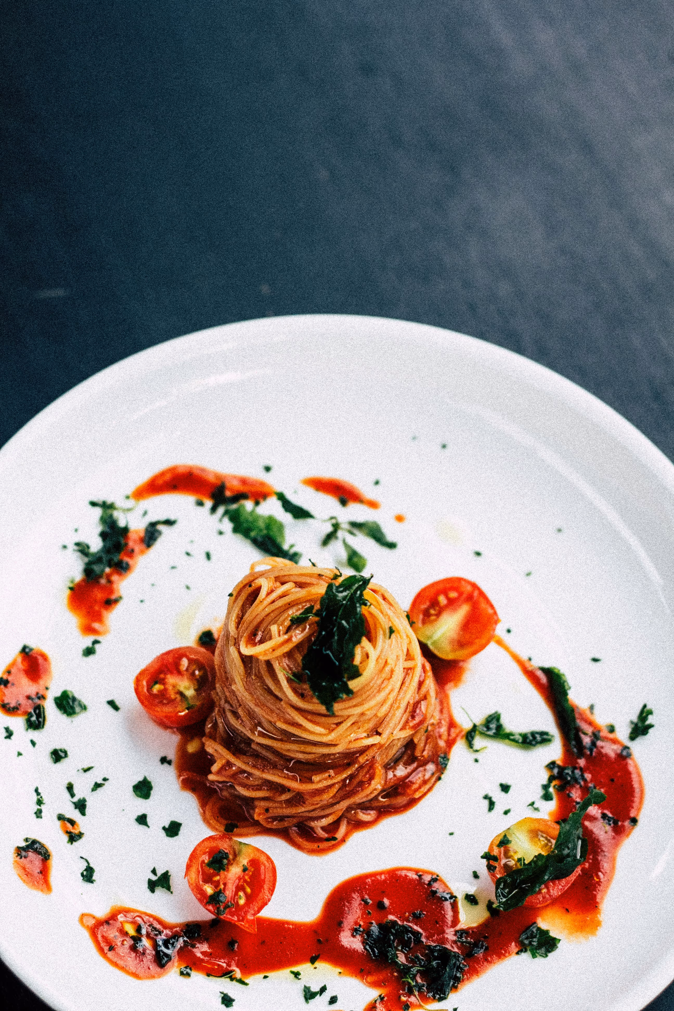 Assiette blanche avec une portion de spaghettis enroulés, garnie de sauce tomate, tomates cerises et herbes fraîches.