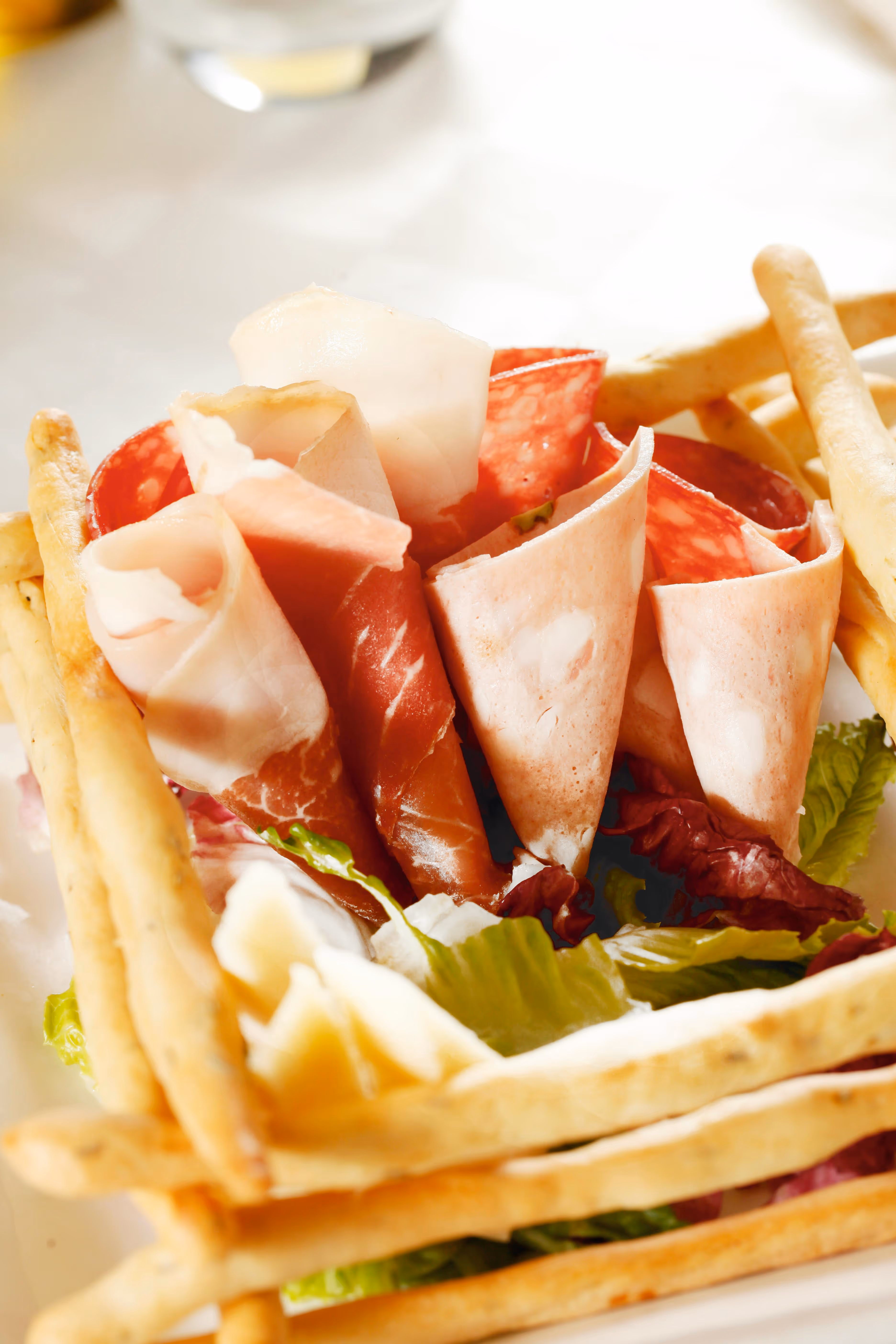 Fines tranches de charcuterie roulées, accompagnées de légumes verts et de gressins croustillants.