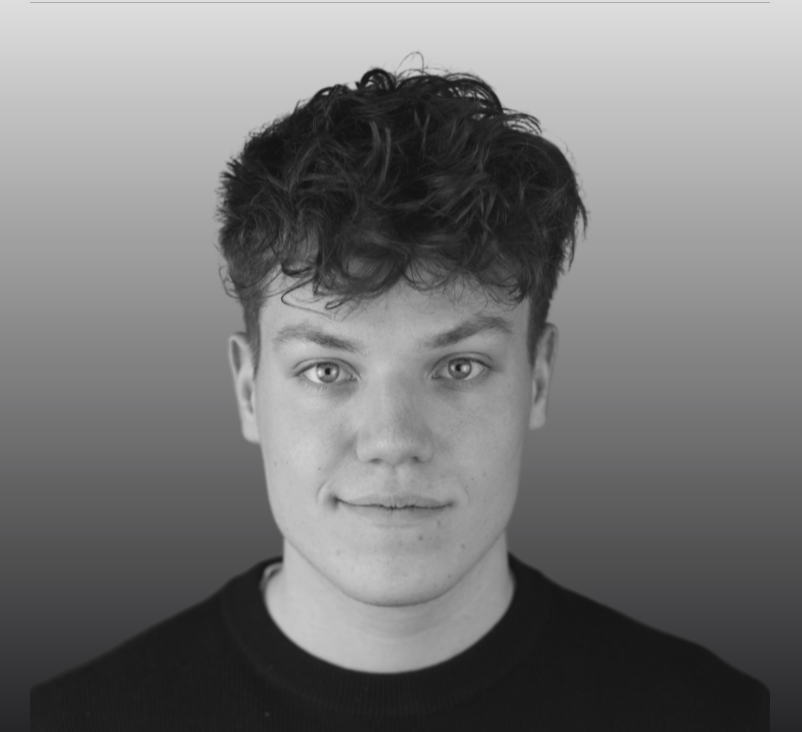 Black-and-white portrait of a young man with curly hair wearing a dark shirt against gradient background.