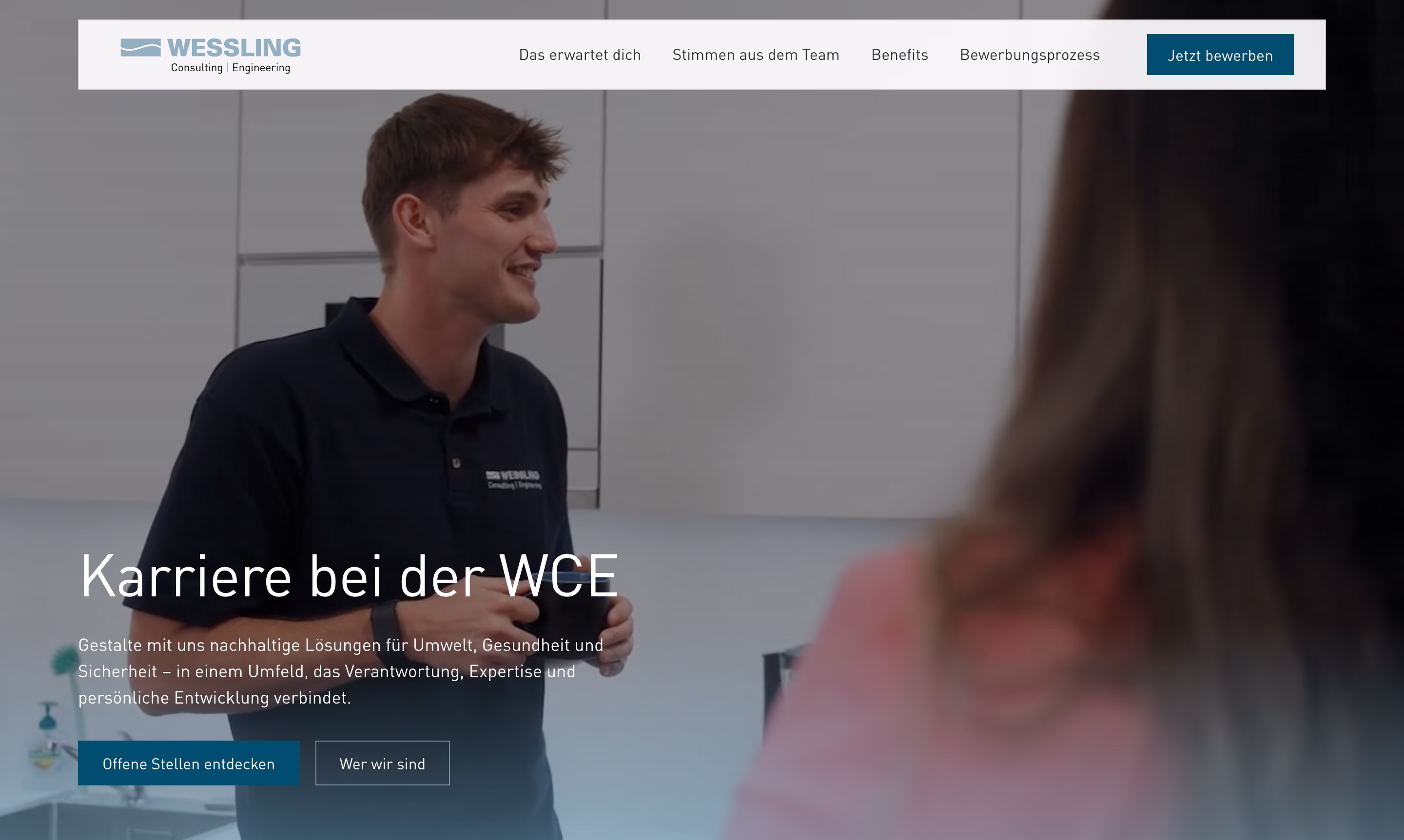 Ein Mann im WESSLING Polohemd spricht mit einer Frau in einem hellen Büro.