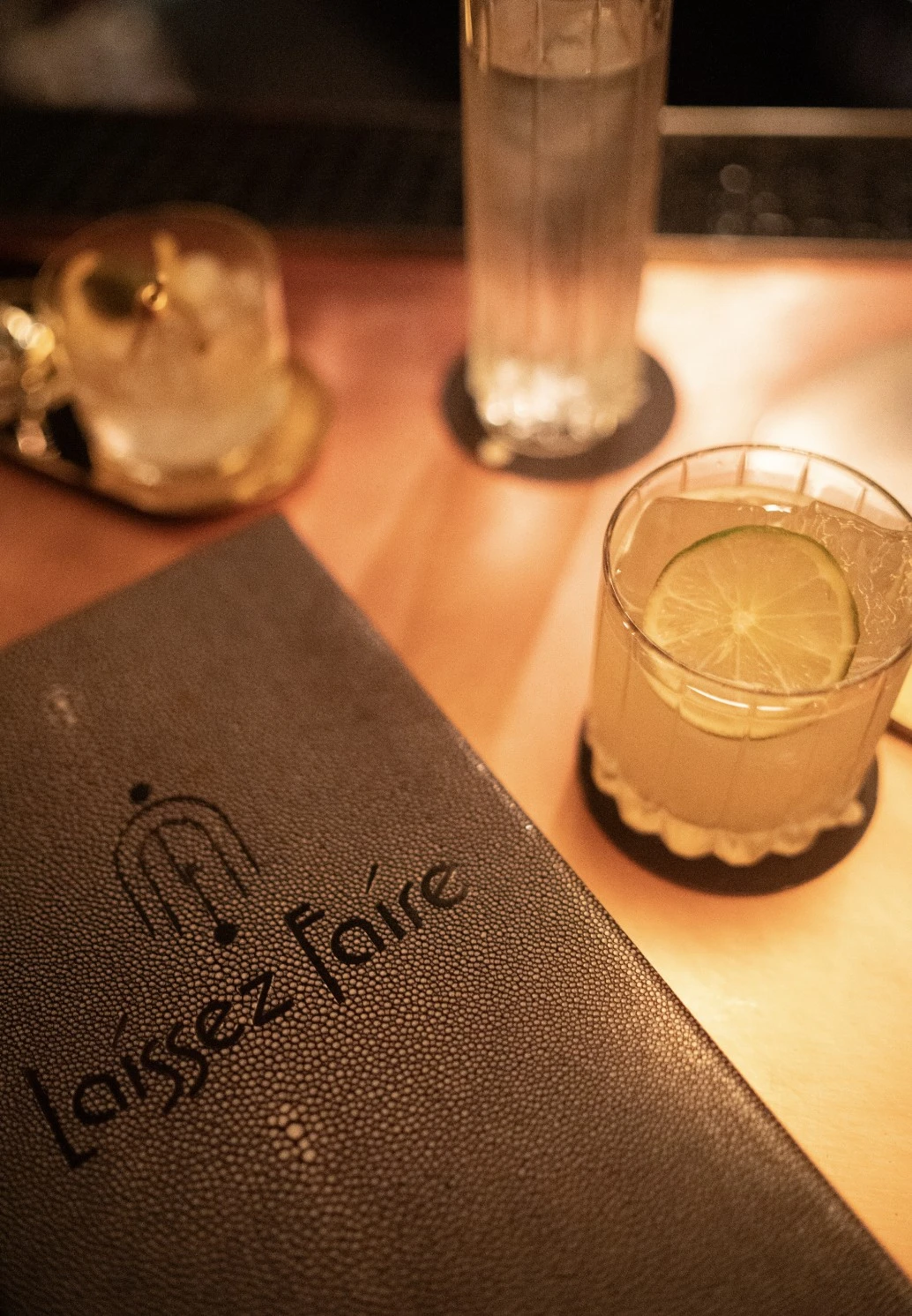 Cocktail menu titled 'Laissez Faire' beside two glasses of cocktails, one garnished with a lime slice.