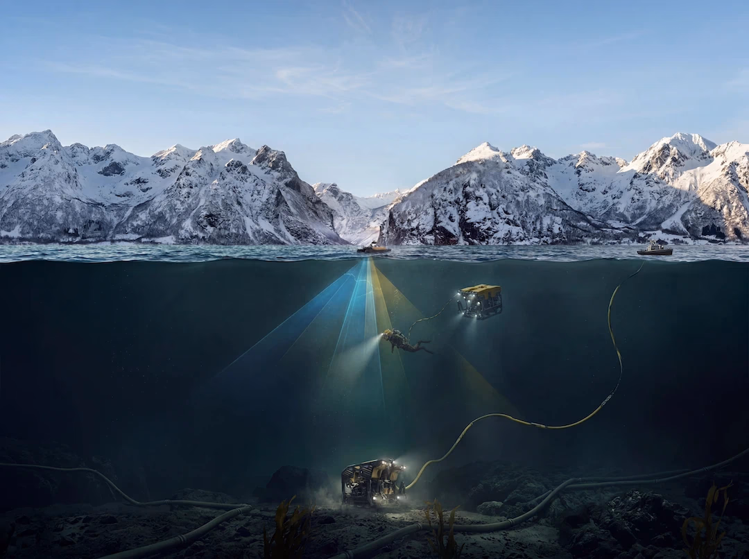 Undervannsutsikt med fjell i bakgrunnen og dykkere med undervannsroboter og lys under vannet.