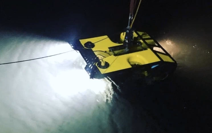 Gult undervannsrobot med lys som lyser i mørkt vann.
