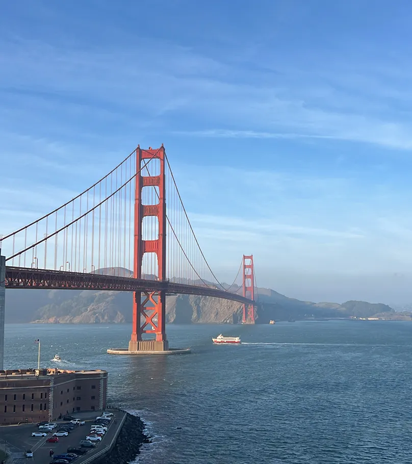 Golden Gate Bridge over blue water under clear sky with boats and land in the background.