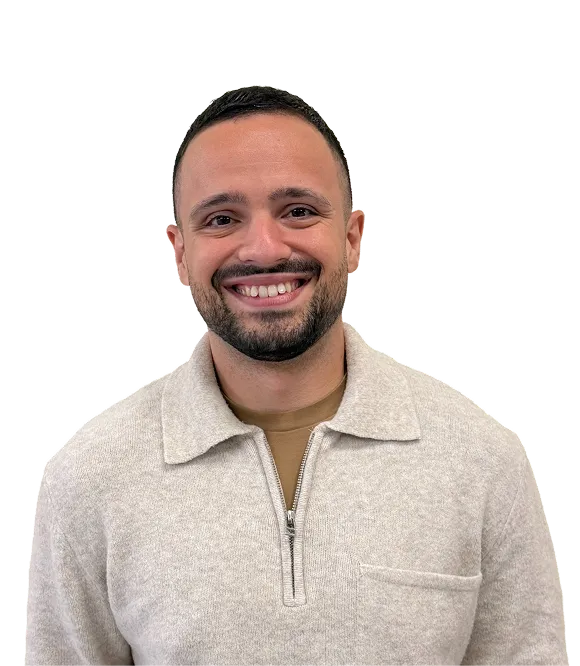 Smiling man with short dark hair and beard wearing a beige quarter-zip sweater over a brown shirt.
