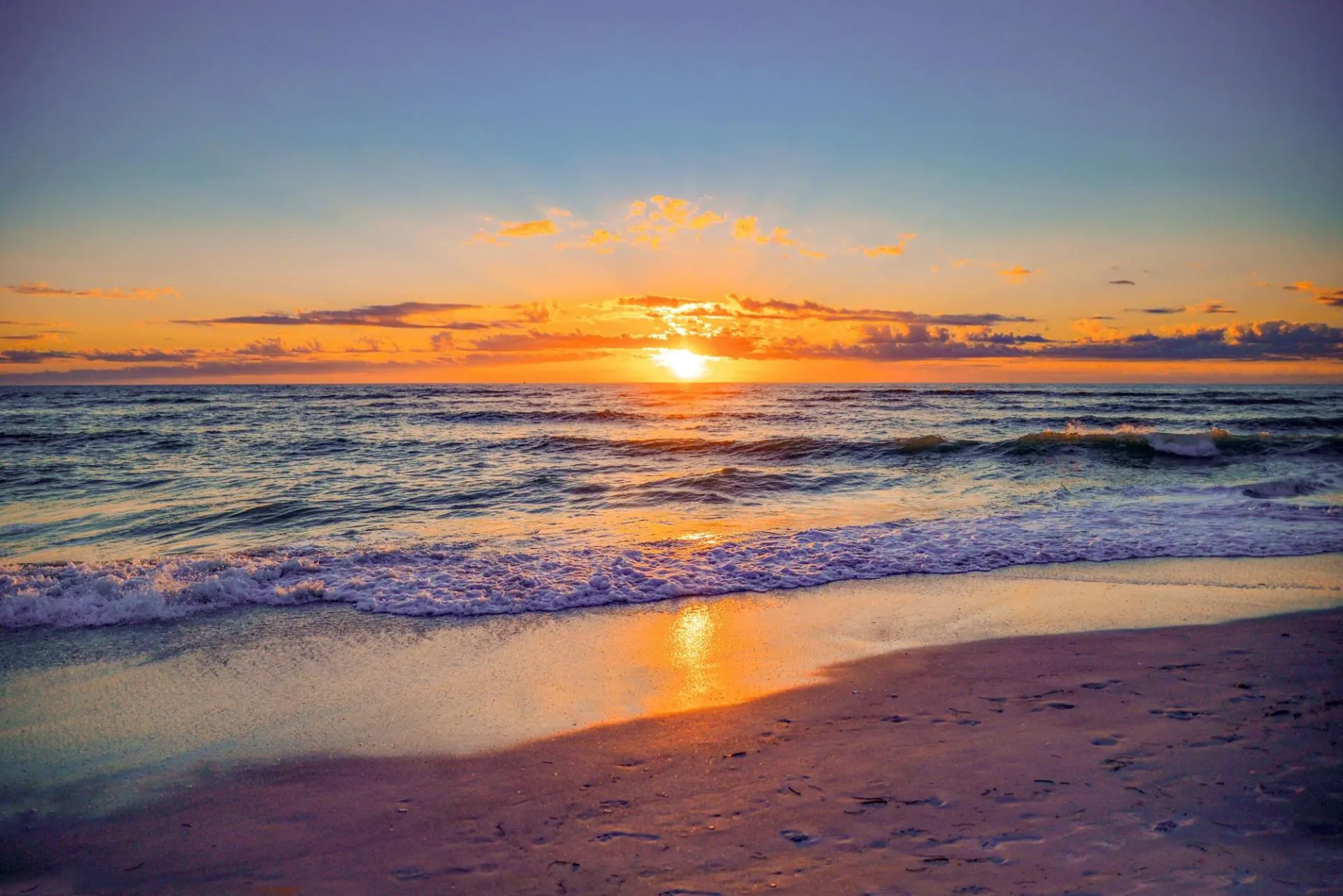 Sunset over ocean waves with a sandy beach in the foreground.