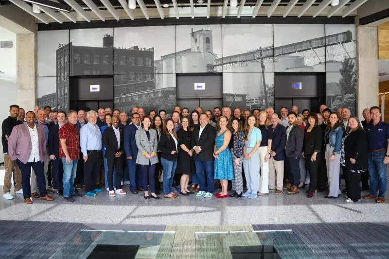 Group photo of diverse professionals standing indoors against a large black-and-white industrial building mural.
