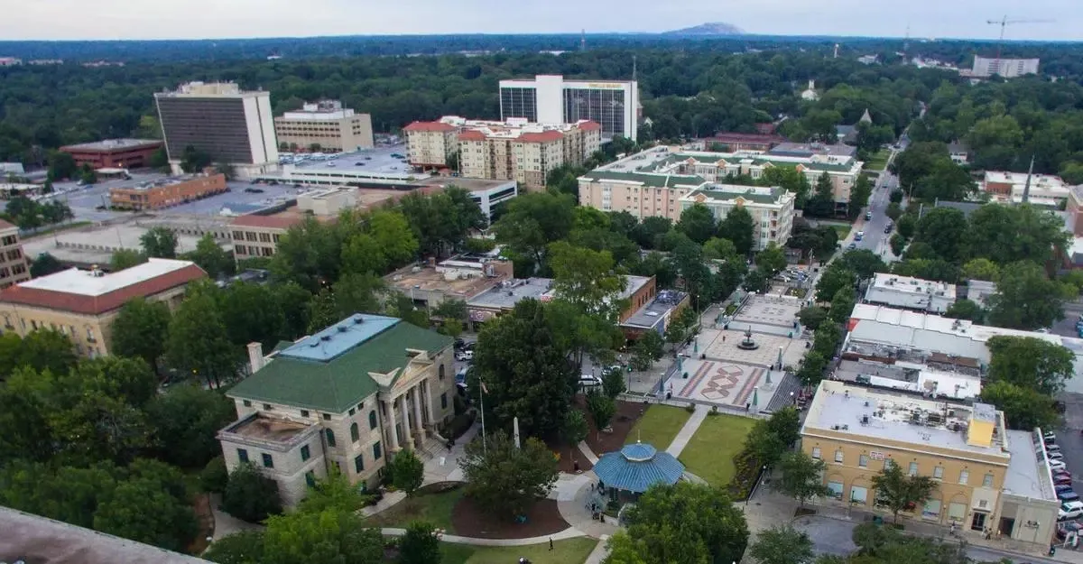 Aerial view of a cityscape with a central park area featuring a gazebo and surrounding buildings amid dense greenery.