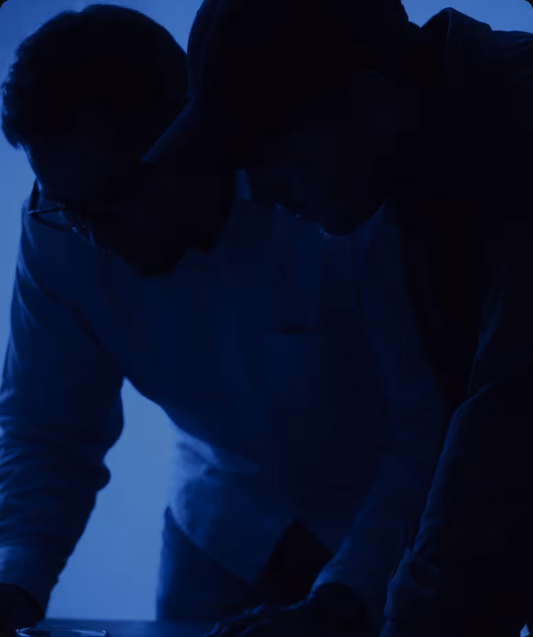 Silhouettes of two people leaning over a table in a dimly lit blue environment.
