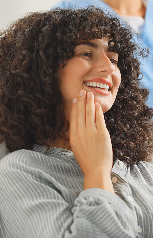 Smiling woman with curly hair touching her cheek, wearing a striped button-up shirt.