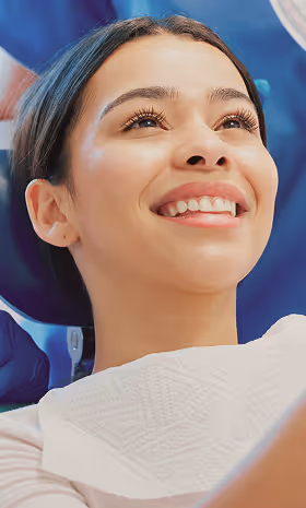 Smiling woman looking upward wearing a dental bib with a dentist in the background.