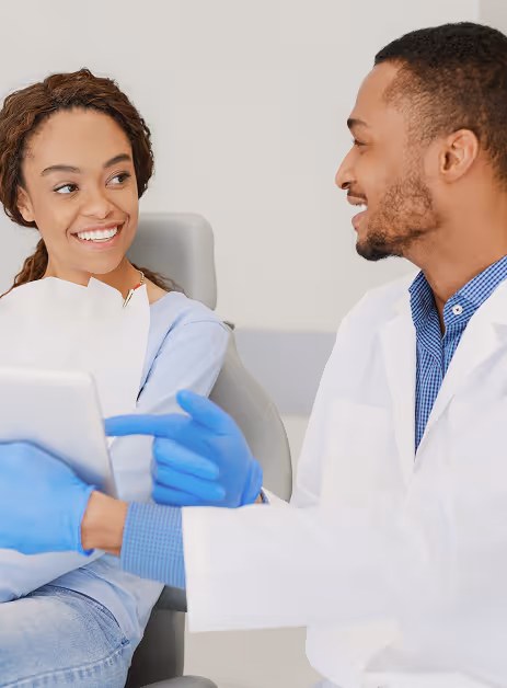 Smiling dentist in gloves talks with woman patient seated in dental chair.
