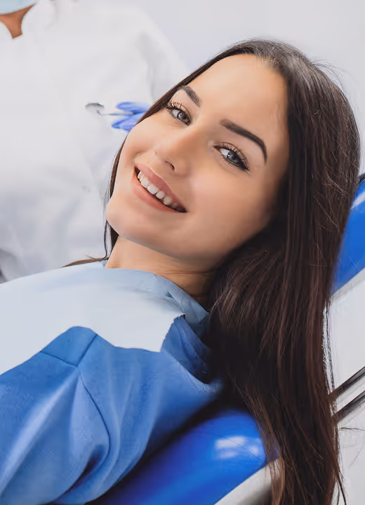 Smiling woman reclining in a dental chair wearing a protective bib during a dental visit.