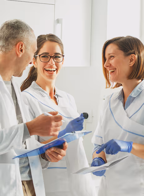 Three medical professionals in lab coats and gloves smiling and discussing notes in a bright room.