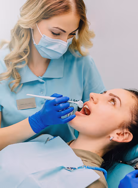 Dentist in mask and gloves examining female patient's mouth with dental tool.