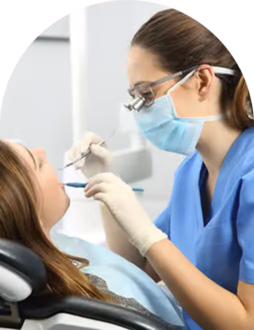 Dentist in blue scrubs and mask examining a patient's mouth using dental tools in clinic.