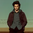 A man standing in front of a fence with his hands in his pockets.