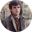 A man in a coat and tie standing in front of a tree.