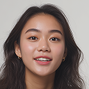 Portrait of a young woman with long dark hair smiling against a plain background.