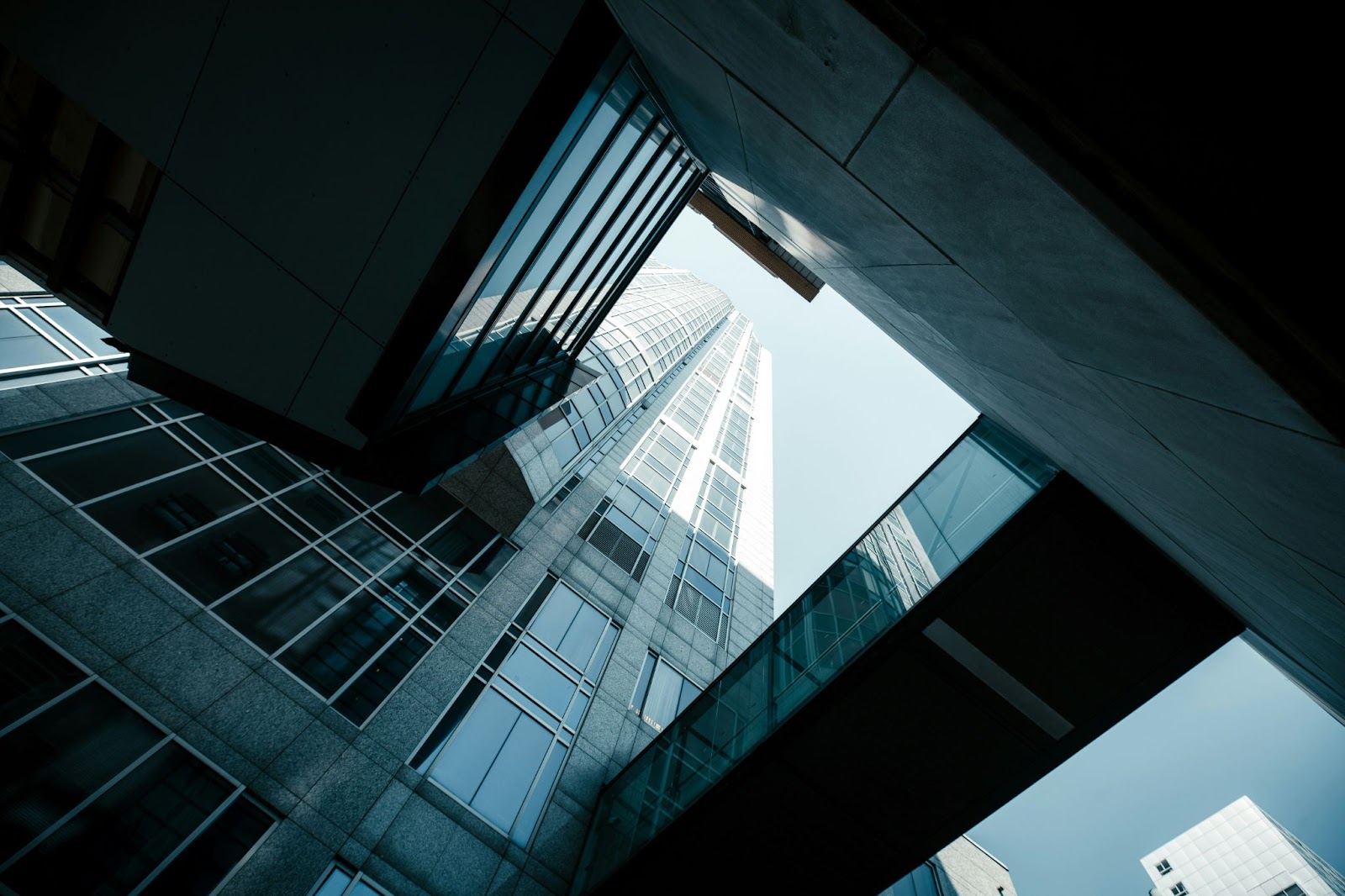 View looking up at modern glass and steel skyscrapers with a glass skybridge between buildings.