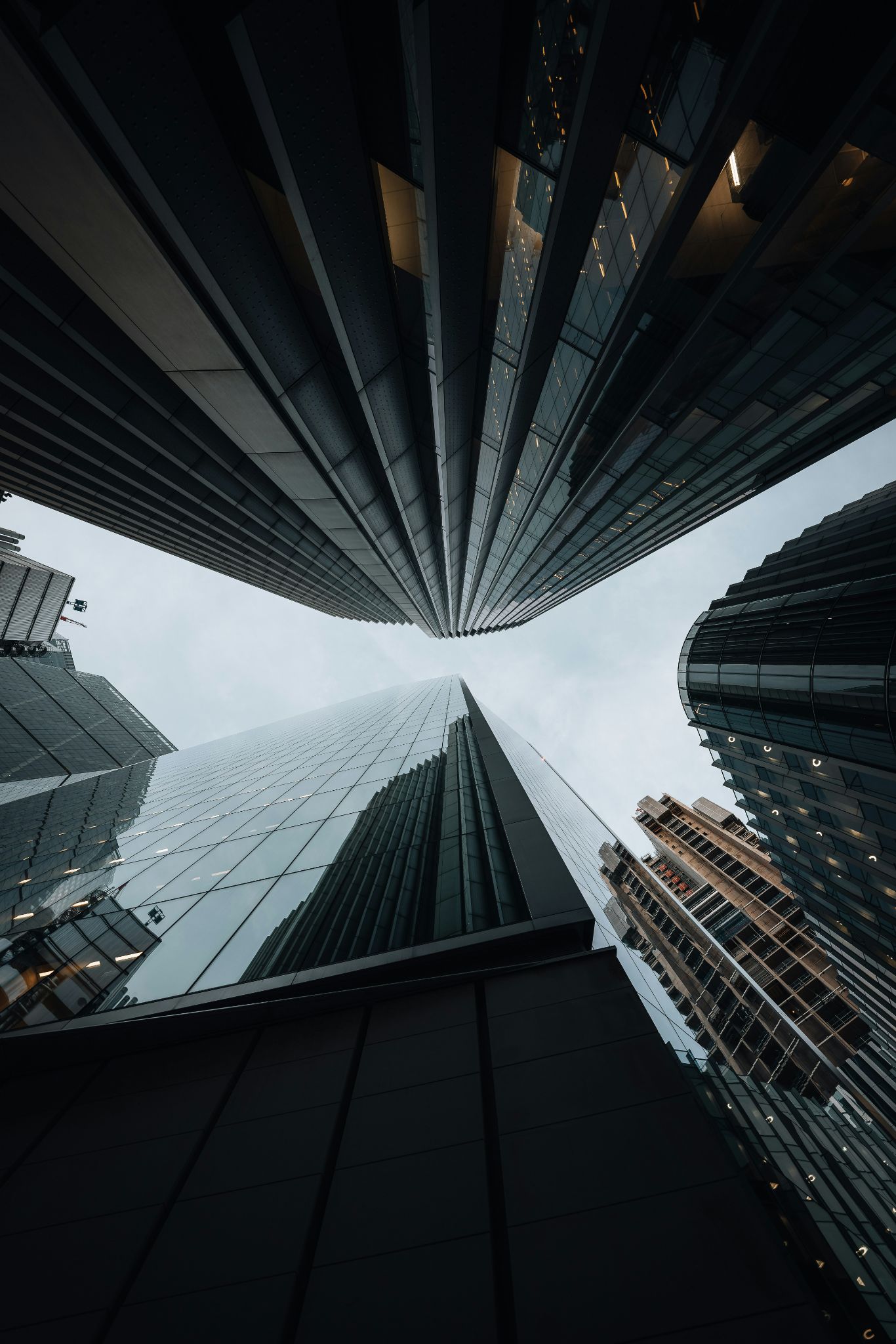 View looking up at tall modern skyscrapers with glass and steel facades against a cloudy sky.