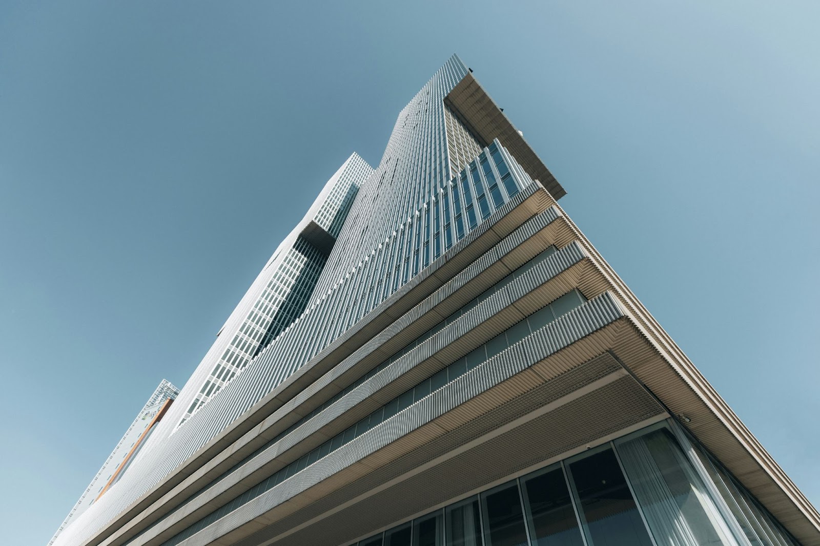 Low-angle view of a tall modern skyscraper with glass windows and architectural metal panels under a clear blue sky.