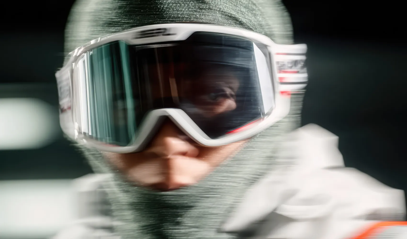 Close-up of a person wearing white ski goggles and a grey balaclava with motion blur effect.