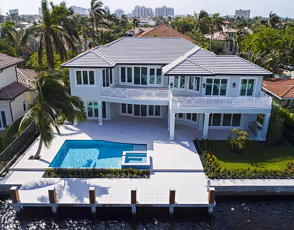 A large white two-story house with a balcony overlooking a swimming pool and a waterfront dock, by MT Construction Group Miami