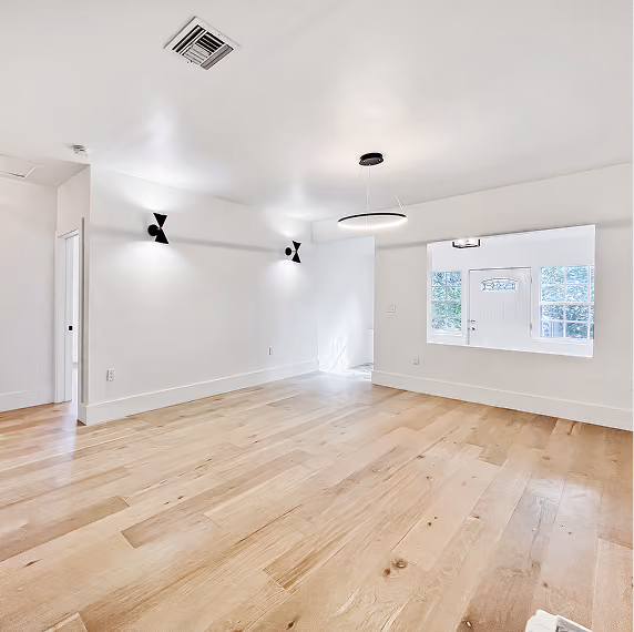 Bright empty room with light wood floor, white walls, by MT Construction Group Miami