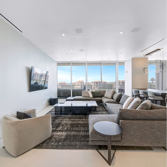 Modern living room with gray sectional sofa, armchair, coffee tables, and large windows showing city view.