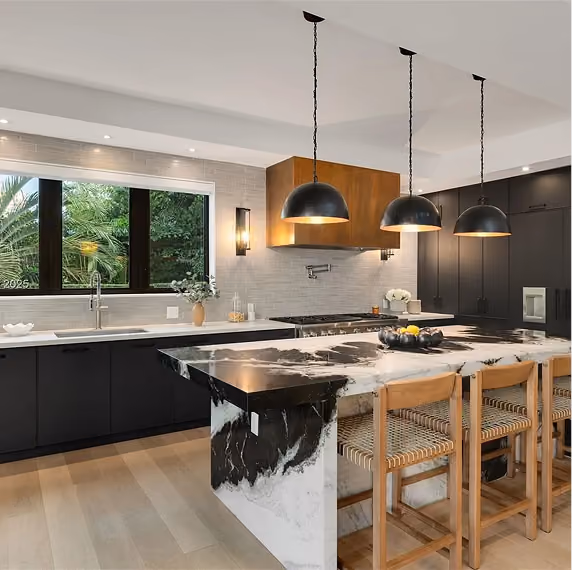 Modern kitchen with black cabinets, marble island, wooden stools, and three black pendant lights.