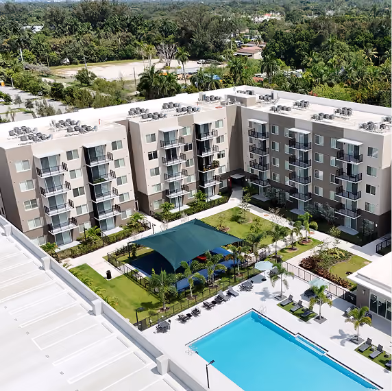 Aerial view of a modern apartment complex with a pool, shaded courtyard, and surrounding greenery.