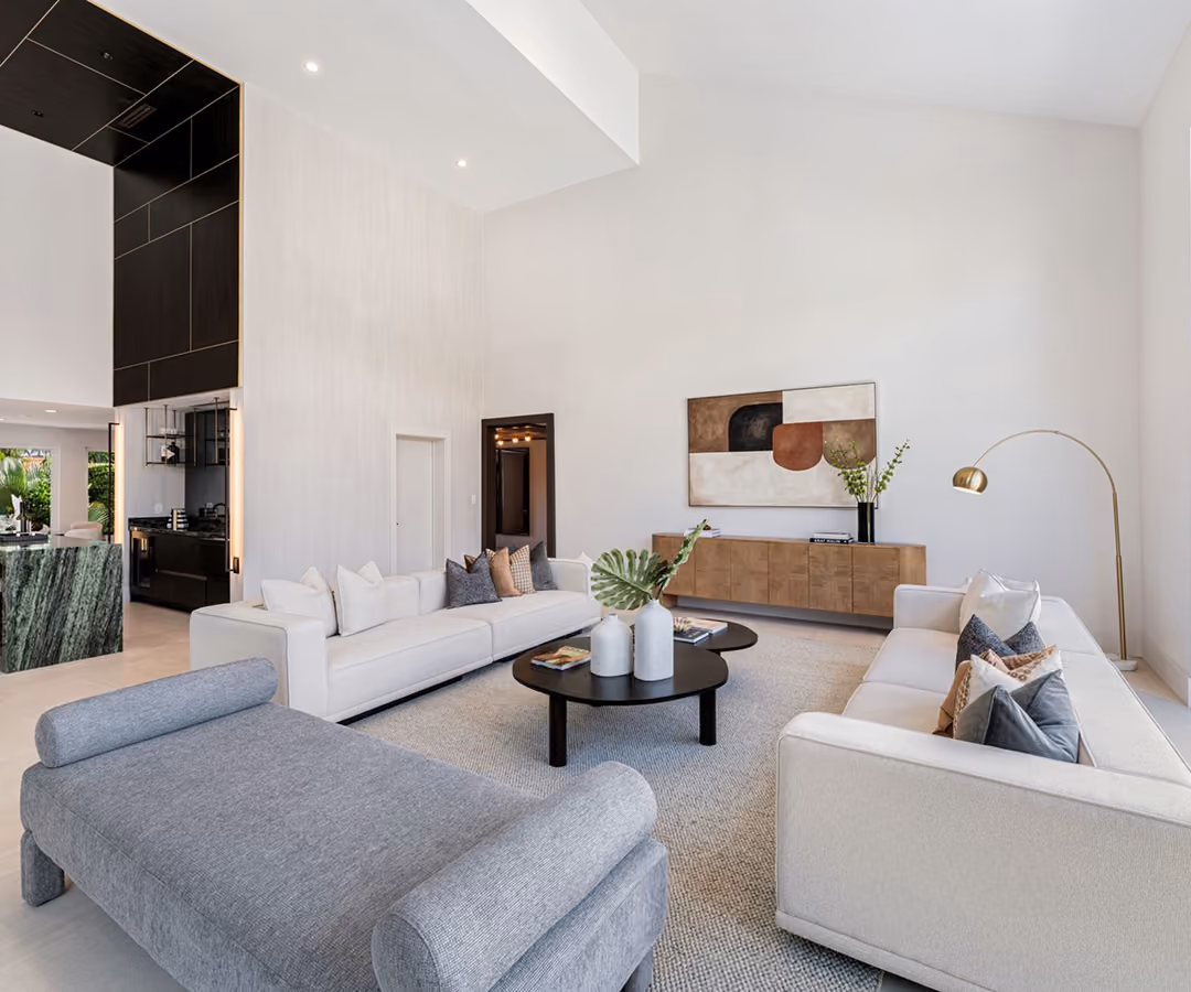 Modern living room with two white sofas, gray chaise, round black coffee tables, and abstract wall art.