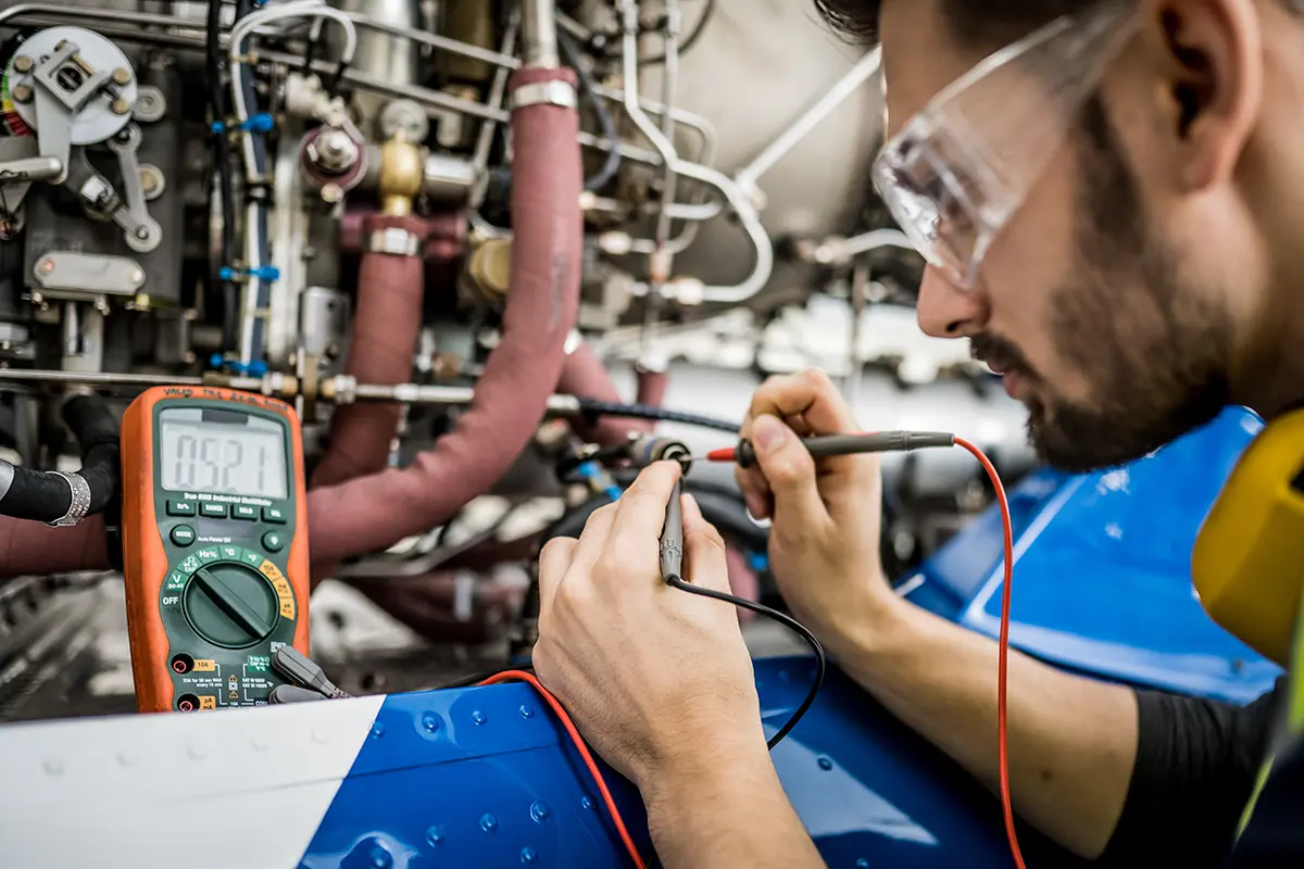 Technician using multimeter probes to test electrical components inside machinery with complex wiring.