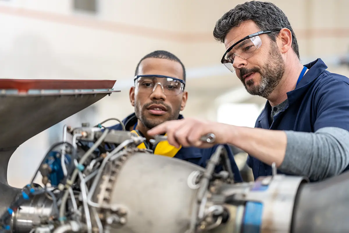 Two male engineers wearing safety glasses inspecting an aircraft engine together.