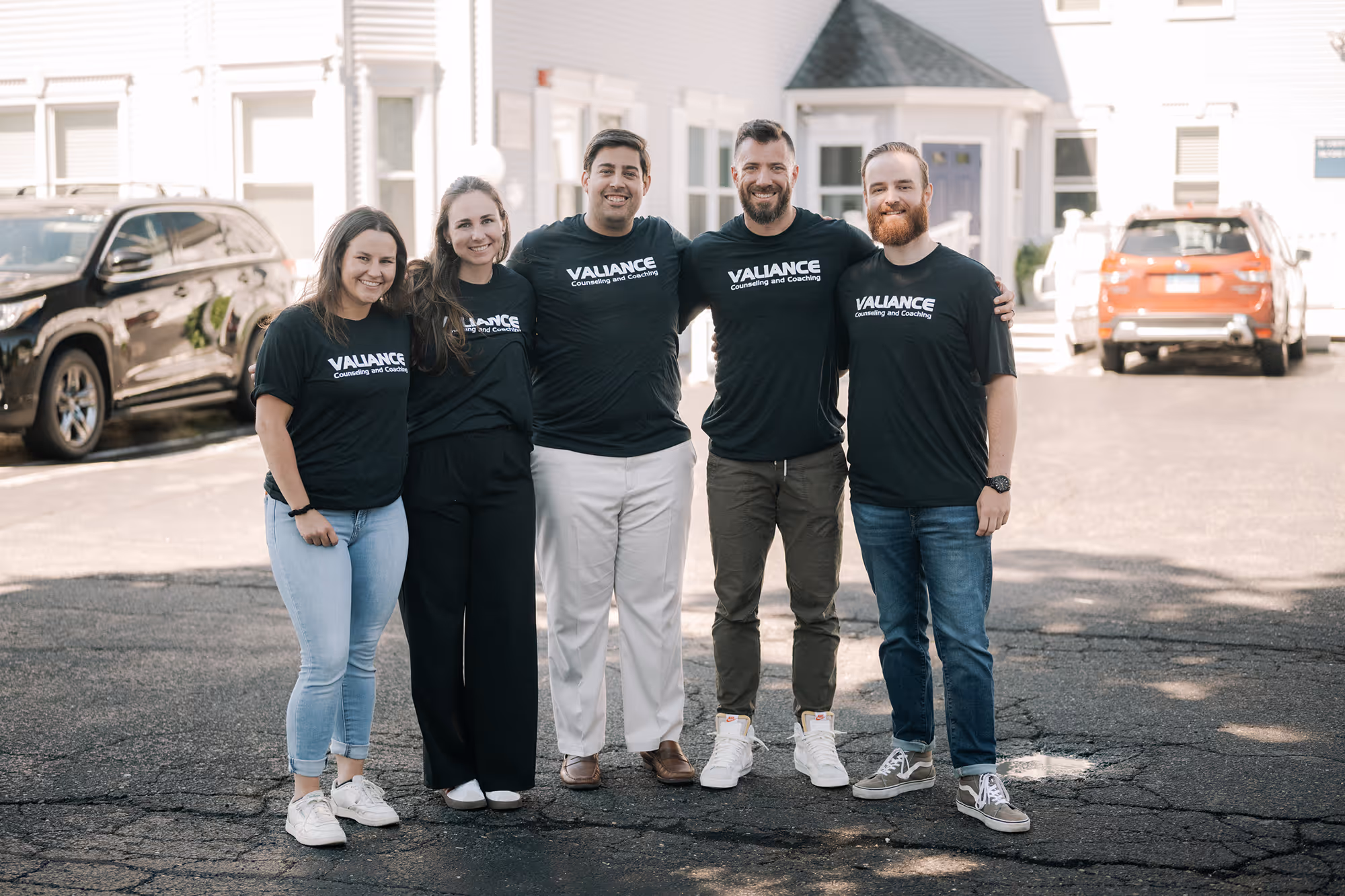Five smiling people standing arm in arm wearing matching shirts that read Valiance Counseling and Coaching.