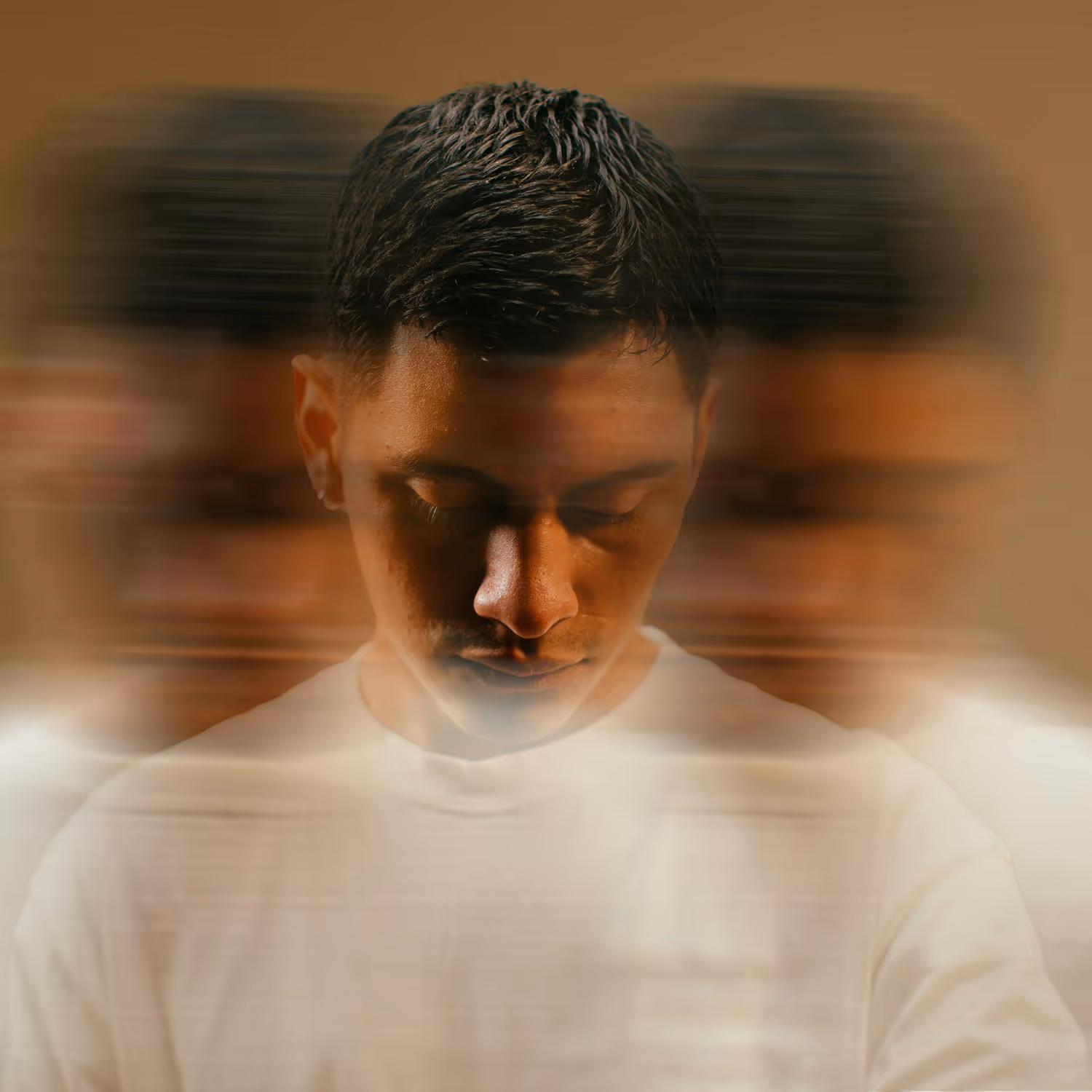 Man with closed eyes and head bowed, multiple blurred ghost images around him on a brown background.