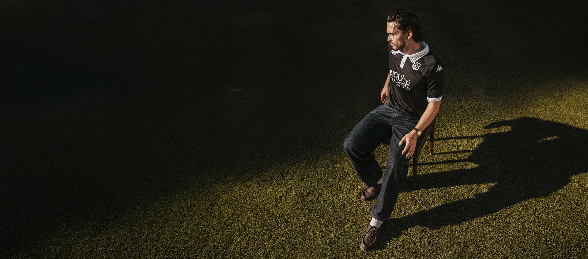 Photo d'un homme assis sur une chaise, sur un terrain de foot, portant le nouveau maillot de La Ligugéenne.