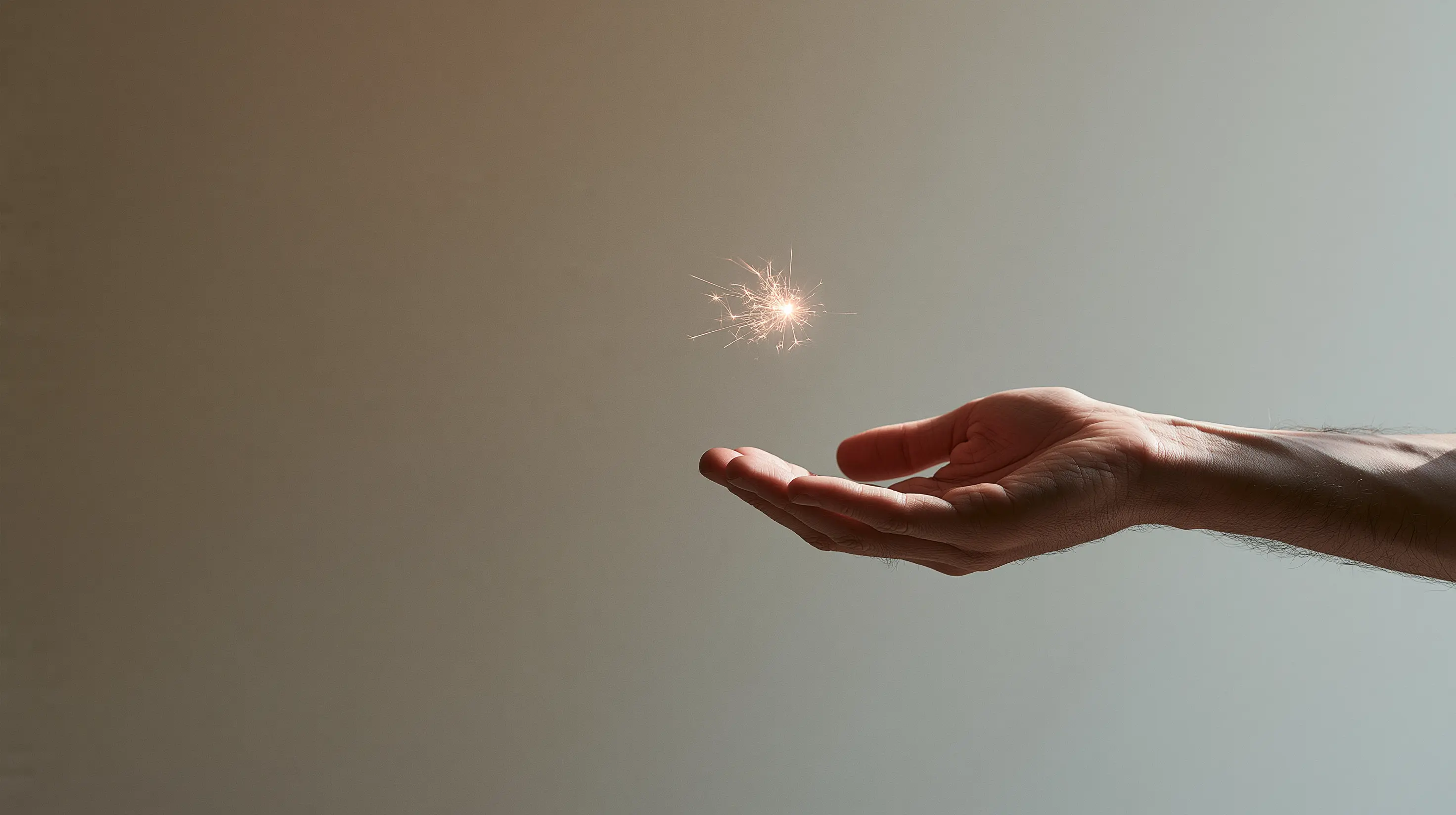 An open human hand with palm facing up, cradling a small bright spark of light against a warm off-white background — conceptual editorial image of human intelligence as the quiet force AI cannot replicate.