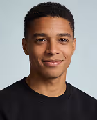 Young man with short curly hair wearing a black shirt smiling against a light blue background.