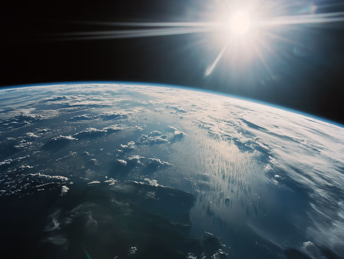 Sun shining over Earth as seen from space with visible cloud cover and ocean.