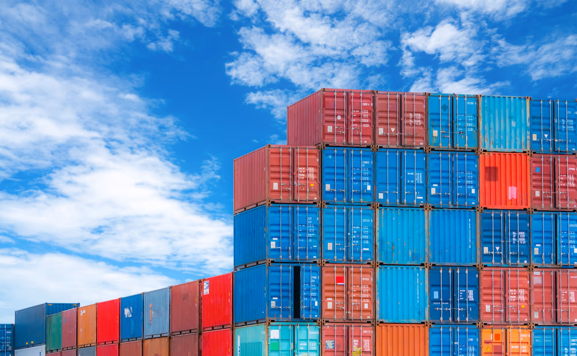 Stack of colorful shipping containers under a partly cloudy blue sky.