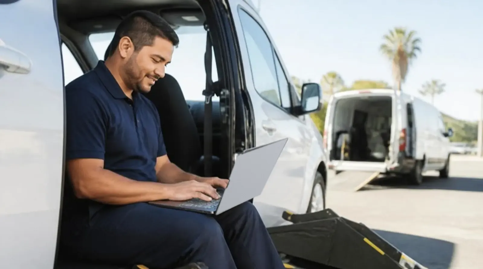 NEMT owner sits in an open van doorway reviewing invoices on a laptop between trips