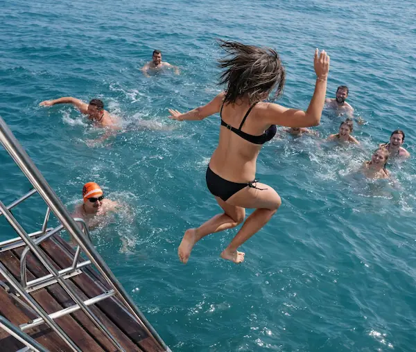 Gente nadando en el mar de Benalmádena y una mujer saltando desde el catamarán Serenity