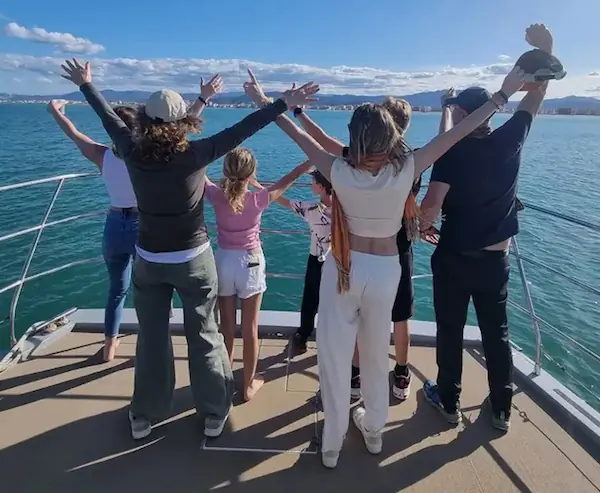Gente de espaldas levantando los brazos en la proa del catamarán Serenity