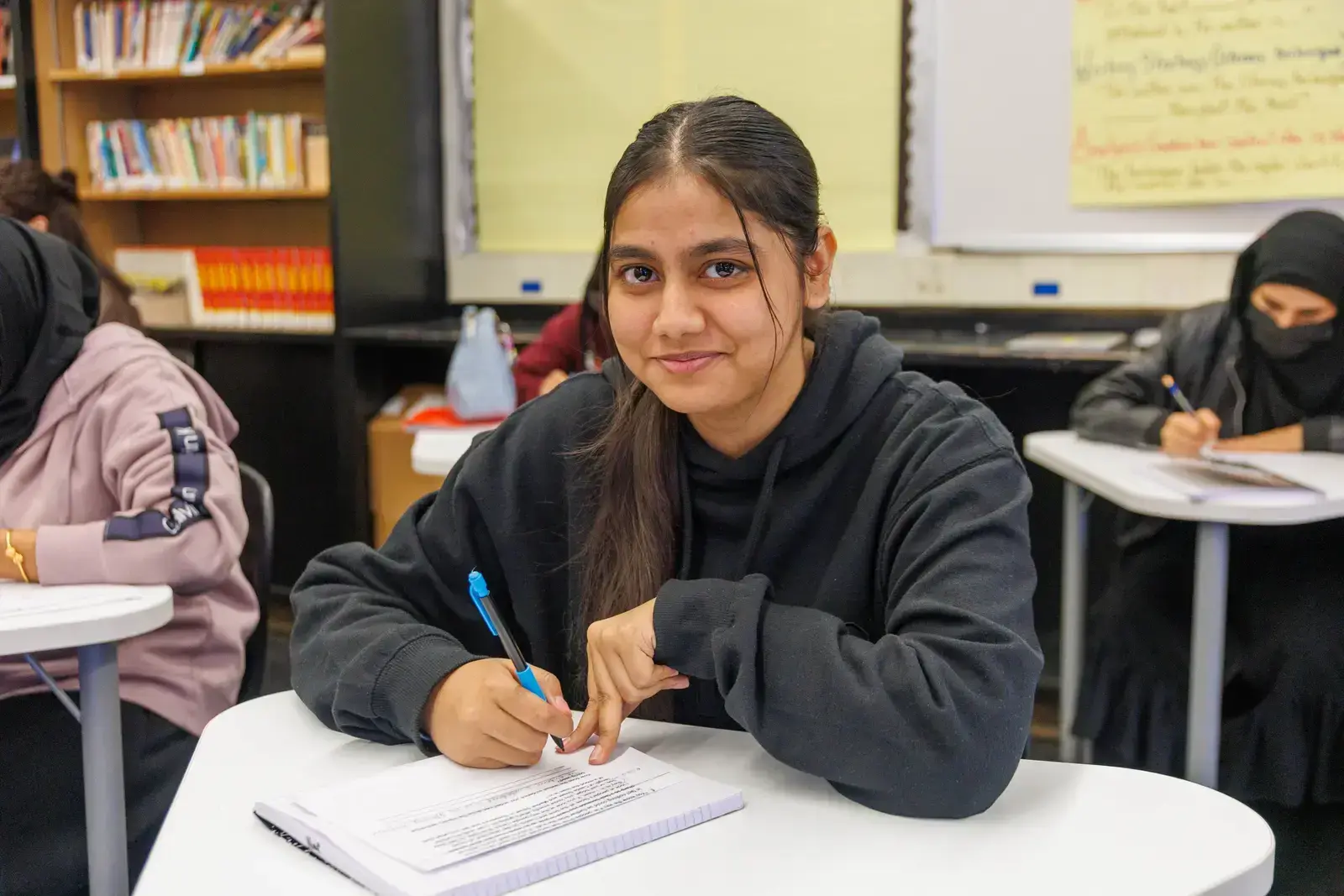 Student smiling while writing at desk in classroom