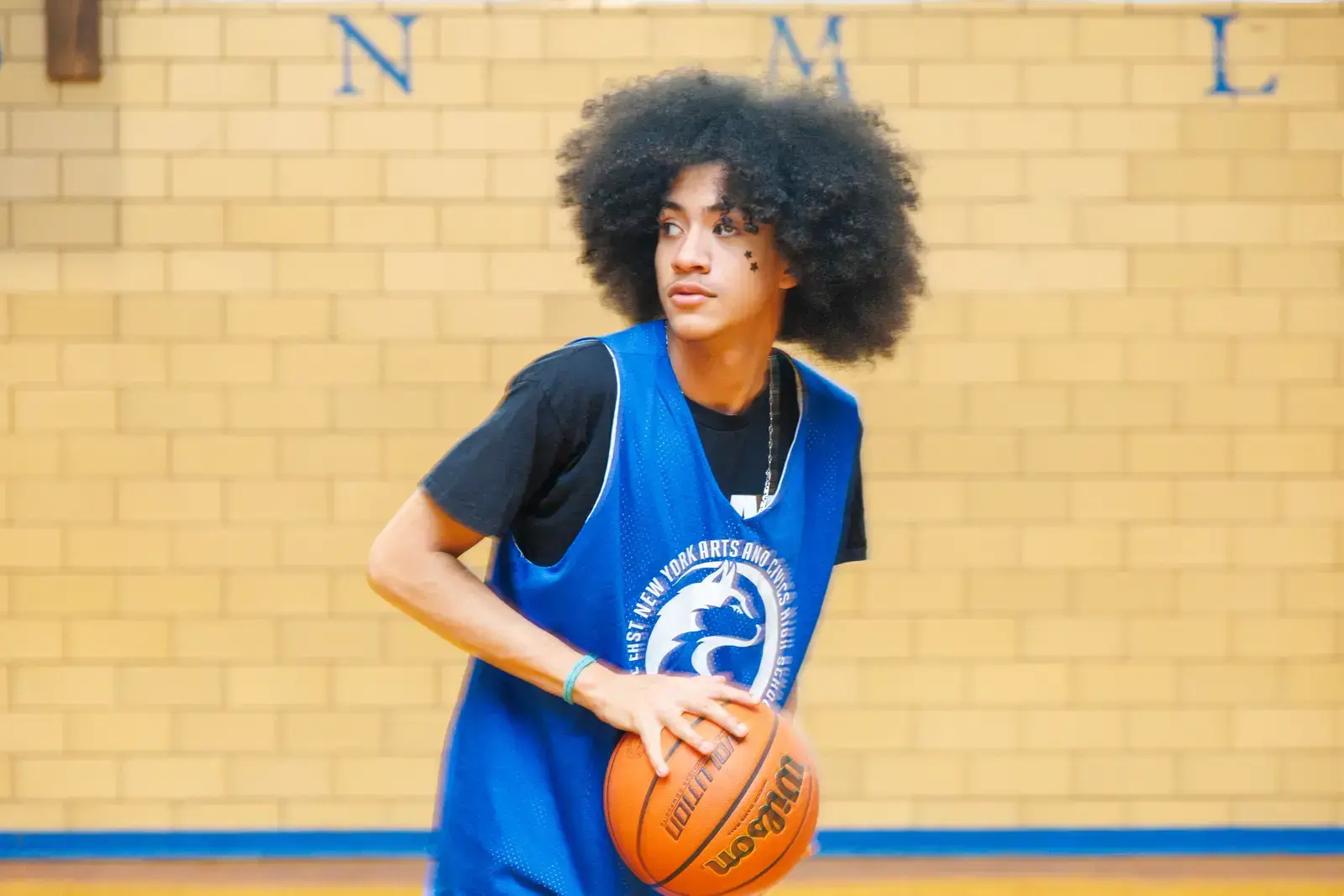 Student in blue school jersey holding a basketball in gym