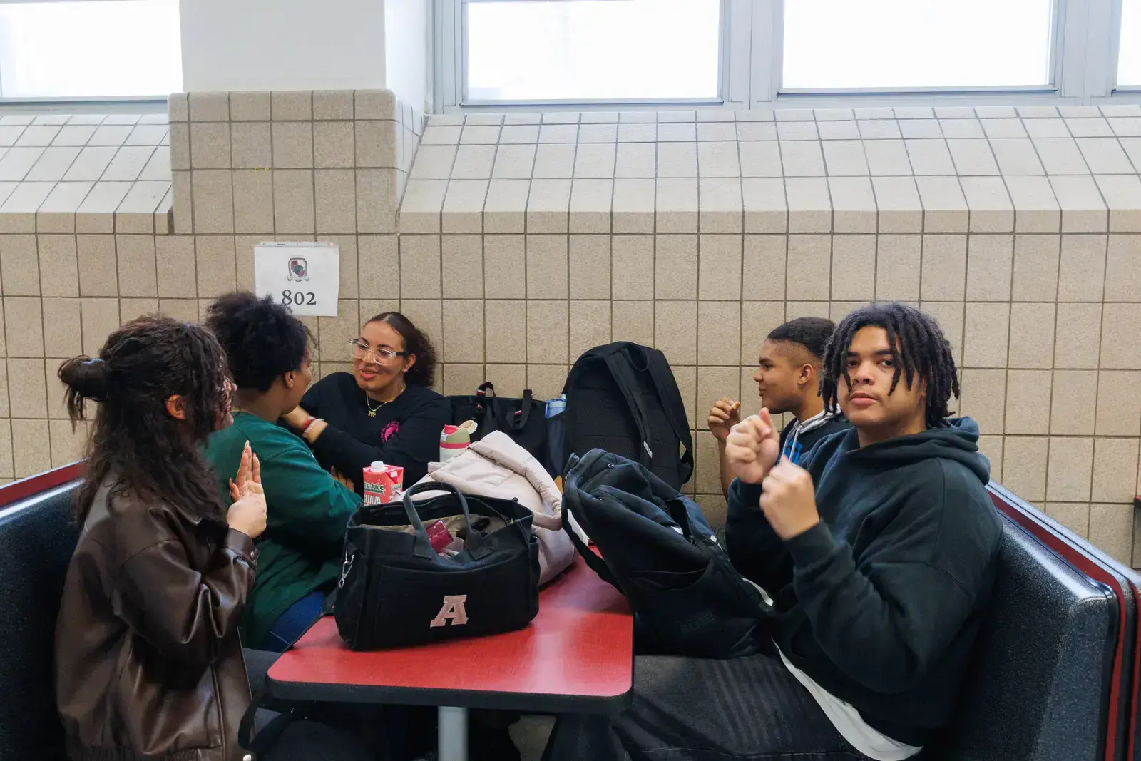 Five high school students socializing together at a cafeteria lunch table